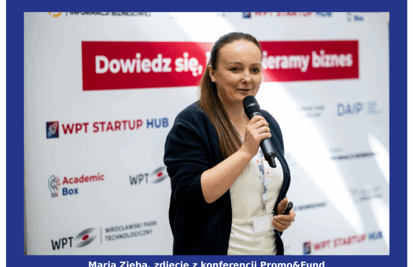 Kobieta, Maria Zięba, ubrana w białą bluzkę i granatowy sweter, trzyma w ręku mikrofon podczas prelekcji na konferencji Promo&Fund